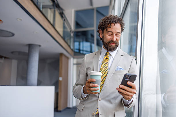 istock Smiling businessman using smartphone and drinking coffee in office 2228939972