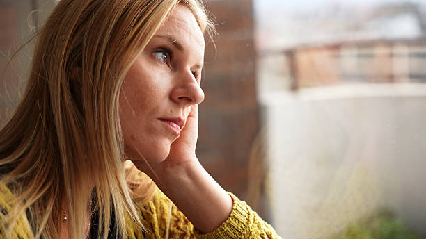 istock Pensive Woman Looking Out the Window During a Gloomy Day 2228942019