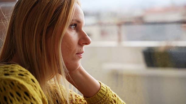 istock Sad Woman Looking Out the Window During a Gloomy Day 2228942041