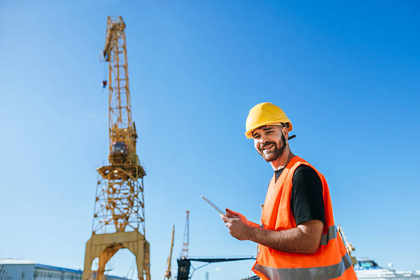 istock Dock worker holding tablet and smiling with crane in background 2228944564