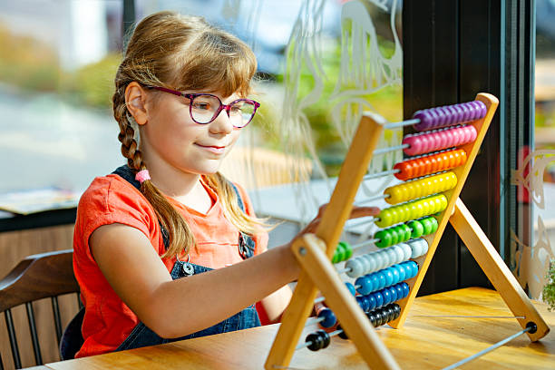istock Adorable elementary school girl with glasses playing with an abacus. Child learning numbers and math. Real life, real people moment of childhood education and early learning 2228944827