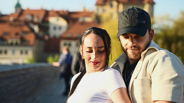 Young Tourist Couple Embracing on Charles Bridge, with the Stunning Prague Castle and Charming Red Roofs Providing a Picturesque Backdrop on a Sunny Spring Day