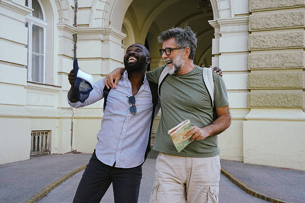 Two cheerful men, one Black and one White, walking together in an urban setting. They chat, laugh, and take selfies with a smartphone. Casual, diverse friendship portrayed in a warm, outdoor city environment. Perfect for themes like tourism, student life, modern friendship, or multicultural connection.