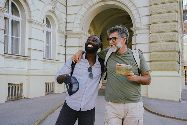 Two cheerful men, one Black and one White, walking together in an urban setting. They chat, laugh, and take selfies with a smartphone. Casual, diverse friendship portrayed in a warm, outdoor city environment. Perfect for themes like tourism, student life, modern friendship, or multicultural connection.
