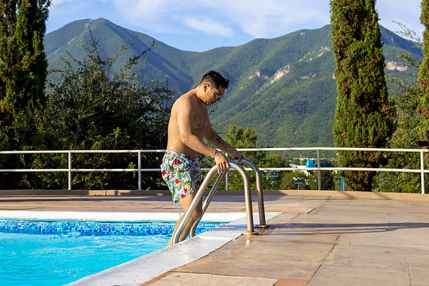 Sitting outdoors by the pool at a holiday apartment, a mid-adult multi-ethnic couple embraces happiness, smiles, and a delightful conversation.