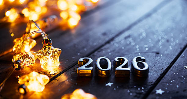 istock Glowing Star Lights and Metallic 2026 Numbers on Dark Wooden Surface 2228957531