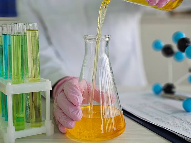 istock Laboratory technician conducts experiment by pouring liquid into a flask with colorful test tubes 2228962437