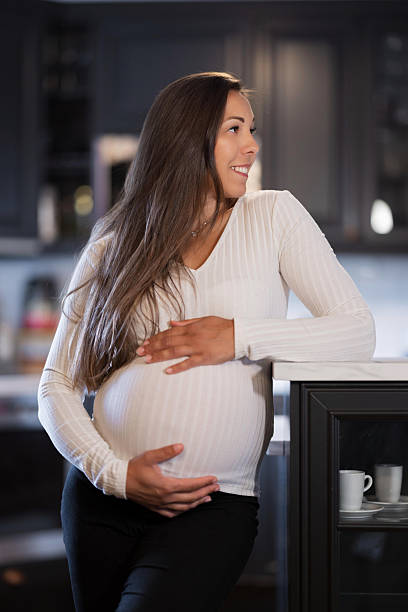 istock Pregnant woman joyfully standing in kitchen, gently holding belly 2228962492