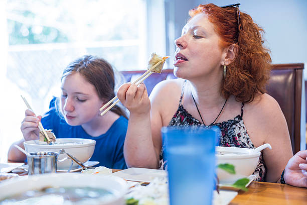 Curly-haired woman eating spring roll with chopsticks. Casual lunch with child at Asian eatery.
