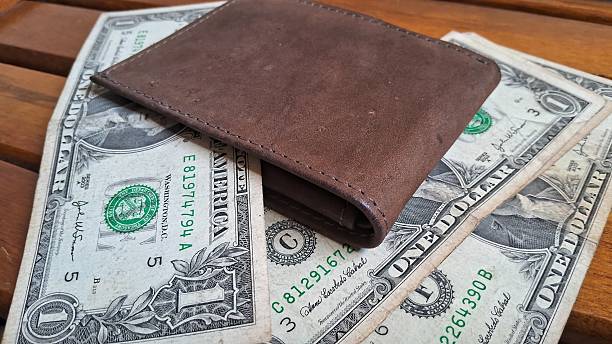 istock Brown leather wallet with US dollar bills on wooden surface 2228967896