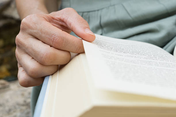 A book with black covers is on a white wooden table. On it is a pair of reading glasses. In the background a lit fireplace invites to moments of relaxed reading.