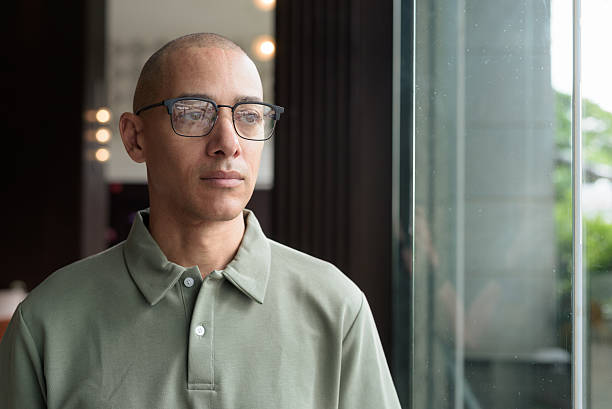 istock Bald Hispanic man looking through window in hotel lobby with eyeglasses, stylish confident portrait 2228977549