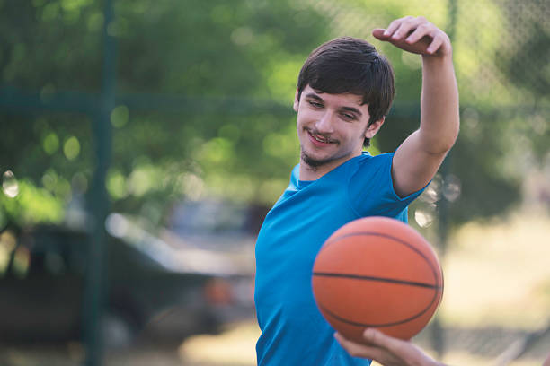 A young man gleefully prepares to shoot a basketball, showcasing enthusiasm and confidence on an outdoor court, radiating energy and vitality in play.
