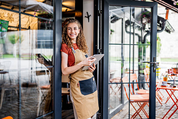 istock Smiling waitress using digital tablet at restaurant entrance 2228983520