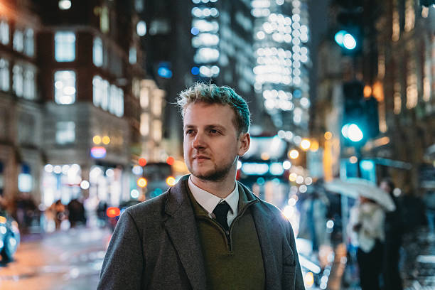 Young businessman walking in London at night, with city lights and traffic in the background