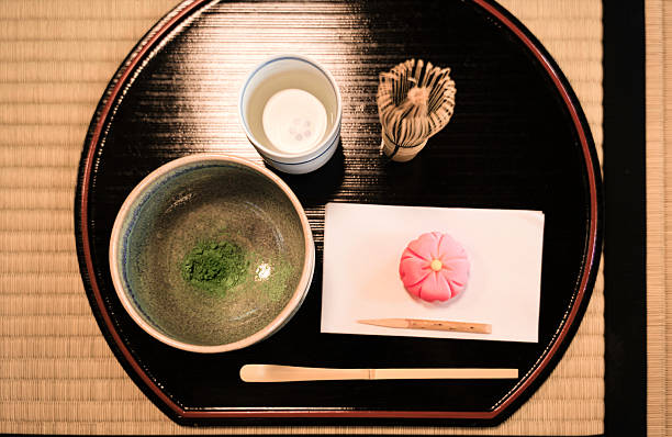 When participating in a traditional Japanese tea ceremony, you encounter a serene and carefully arranged setting. In front of you, there is a tatami mat laid out with a variety of beautifully crafted utensils and dishes. You see a teapot, often made of cast iron or ceramic, as the host pours hot water into a bowl. Using a bamboo whisk, they skillfully froth the matcha powder, creating a vibrant green tea with a rich, frothy top. Nearby, there’s a small tray with a delicate, flower-shaped sweet that balances the bitterness of the tea with a touch of sweetness. The presentation is simple yet elegant, emphasizing natural materials and meticulous craftsmanship. The entire scene exudes calmness, mindfulness, and respect, reflecting the essence of the tea ceremony-an artful ritual of hospitality, harmony, and appreciation for the moment.