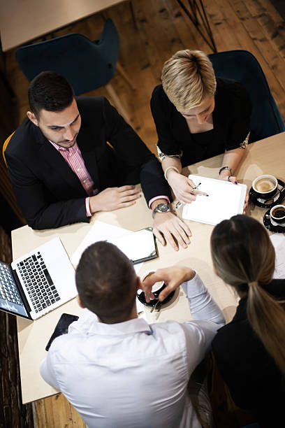 istock Four professionals collaborate at a wooden table with laptops and coffee, showcasing teamwork in a modern, casual office environment. 2229010689