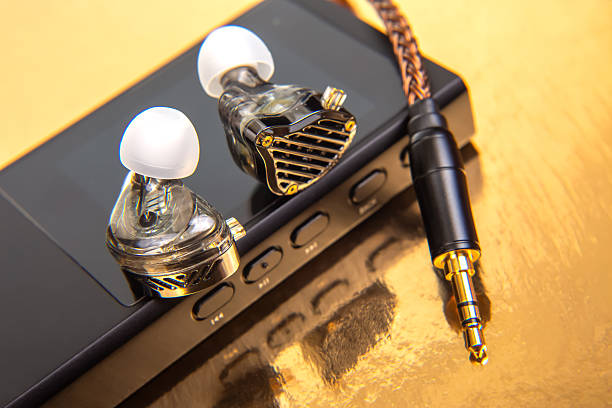 istock Wired earbuds with a woven cable on a black audio device, set on a glossy gold background. Ideal for music lovers, tech enthusiasts, and product shots. High-res photo. 2229020639