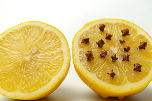 Two lemon halves, one studded with cloves, showcasing a natural insect repellent on a white background