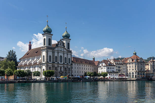 Swiss flag waving in the wind mounted on a ferry, Lake coast with buildings and trees and blue cloudy sky