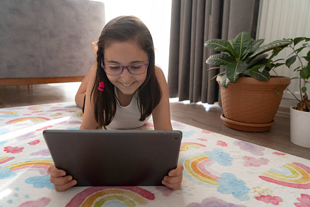 istock Little girl using a digital tablet while lying on the floor at home 2229027413