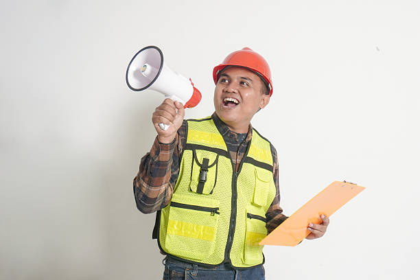 istock Asian construction worker wearing safety vest and helmet, holding project paper plans while announcing through a megaphone, promoting with enthusiasm for marketing 2229029899