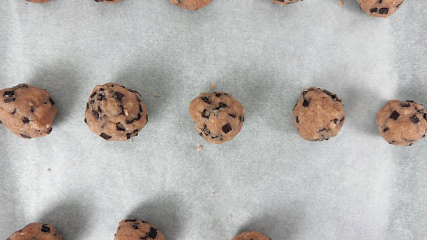 istock Closeup of raw cookie dough balls with chocolate chips arranged on parchment paper before baking during chocolate chip cookie preparation process 2229033021