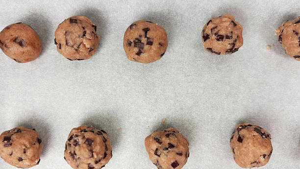 istock Closeup of raw cookie dough balls with chocolate chips arranged on parchment paper before baking during chocolate chip cookie preparation process 2229033022