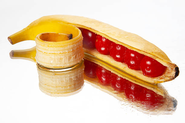 A banana peeled open to display cherry tomatoes nestled inside, captured on a reflective white backdrop. Great for imaginative food visuals, nutrition themes, or playful culinary concepts