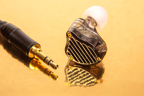 istock A single earbud with a white tip, a 3.5mm audio jack, and a black audio device on a reflective gold surface. Ideal for tech and audio themes. 2229033164