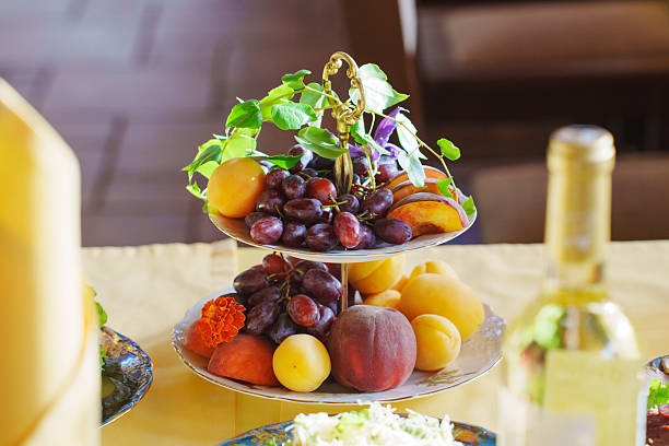 A beautifully arranged two-tiered stand holds an assortment of fresh fruits, including grapes, peaches, and apricots. The colorful display enhances the inviting atmosphere of the gathering.