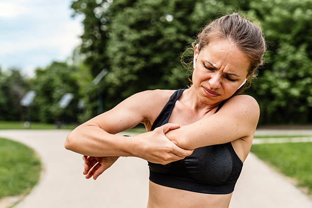 istock Female runner standing and holding painful elbow with pained expression during outdoor workout 2229036032