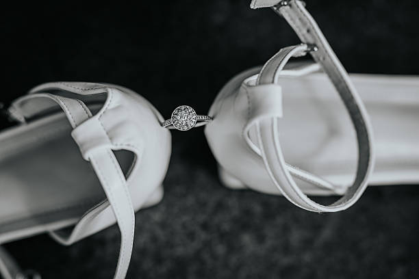 istock Black and white close-up of a diamond engagement ring placed between elegant white bridal shoes, symbolizing love, marriage, and commitment. 2229037061