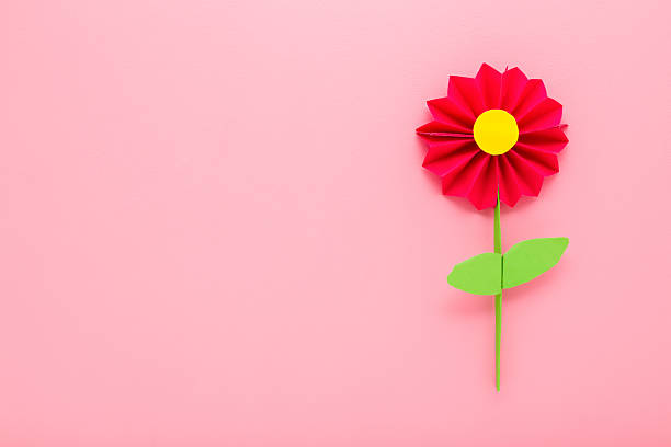 Red flower with green leaves created from colorful application paper on light pink table background. Pastel color. Closeup. Empty place for text. Top down view.