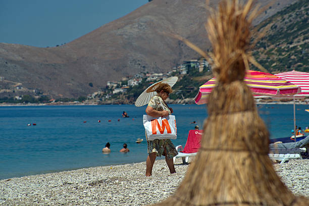 Albania, Borsh beach, July/13/2025 : A tourist leaves the beach protected from the sun by a Chinese paper umbrella.