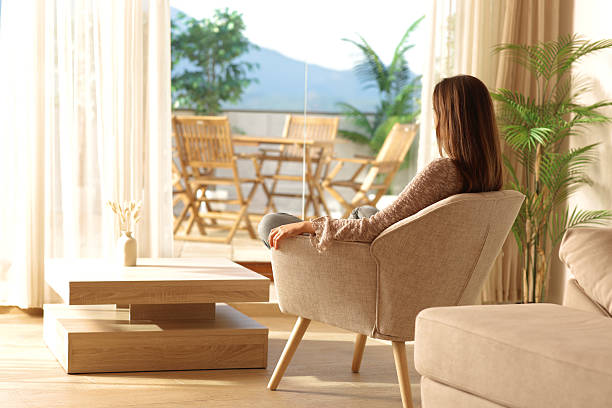 istock Woman sitting on armchair looking through a window relaxing 2229042337