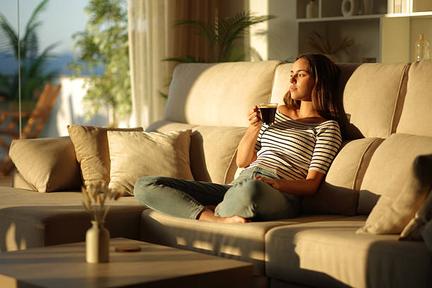 istock Woman drinking coffee at sunset relaxing on a couch at home 2229042431