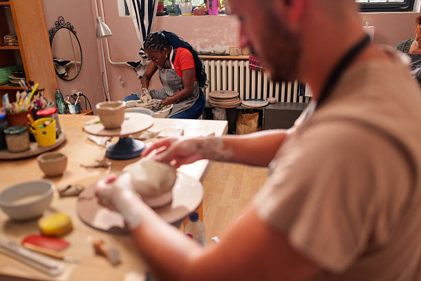 istock Two ceramists working diligently in a pottery workshop, molding clay on a pottery wheel and skillfully shaping a vase, surrounded by various tools and materials 2229045763