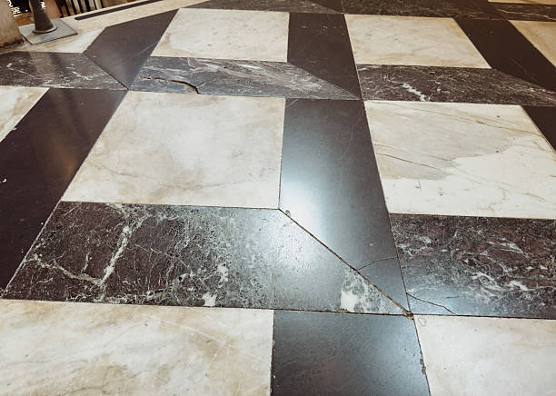 Worn geometric marble floor pattern with black and beige tiles in historical building interior, ancient architecture texture detail