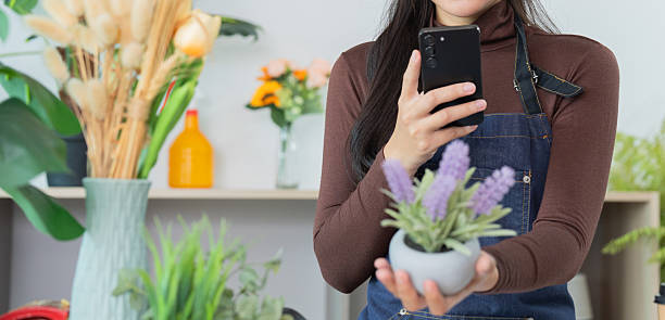 istock Smart Gardening. Woman using smartphone while holding potted plant in modern indoor space. 2229048702