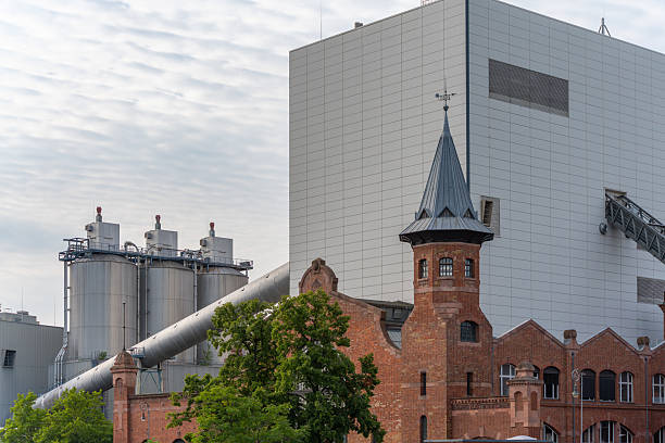 Brick building with modern factory. A red-brick building with a tower stands next to a modern industrial facility. Historic and contemporary architecture contrast strongly.