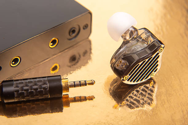 istock An earbud, a 3.5mm audio jack, and a black audio device on a gold surface, great for showcasing tech accessories and sound equipment. 2229051703