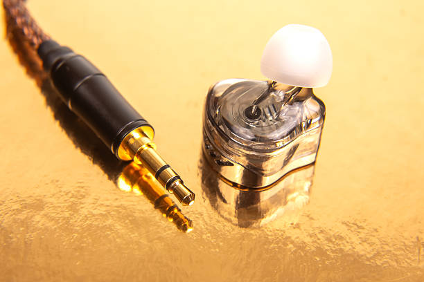 istock A single earbud, a gold-plated 3.5mm jack, and a black audio device on a reflective golden surface, ideal for tech product shots and audio themes. 2229051750