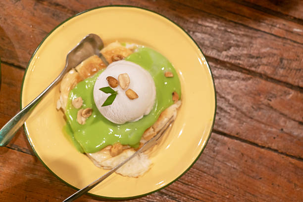 A mouthwatering dessert featuring a scoop of ice cream atop a sweet green sauce with banana and nuts. Perfect for any occasion or culinary adventure.