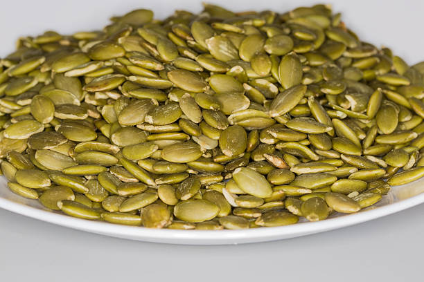 Heap of the dry pumpkin seeds peeled from their shells on dish, front view close-up in selective focus