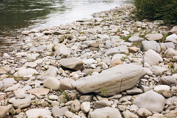 Pebble riverbank near a clear mountain stream with fresh water and lush green surroundings.