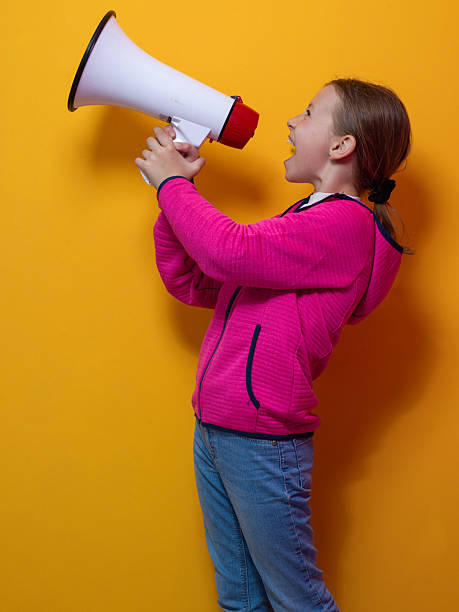 istock Excited girl shouting into megaphone against orange background 2229058913