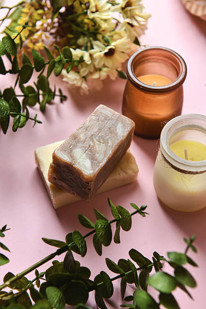 close-up, a piece of handmade soap on scattered orange bath salts in the form of small balls, surrounded by white rose petals, dried flowers, towels twisted into a roll, and candles