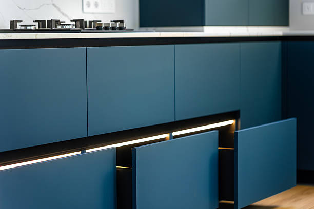 Matte blue base cabinets with a continuous LED strip under the countertop, open drawers guide the eye toward the gas cook top.