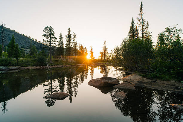 A silhouette of the landscape as the first light breaches the horizon at a mountain lake.